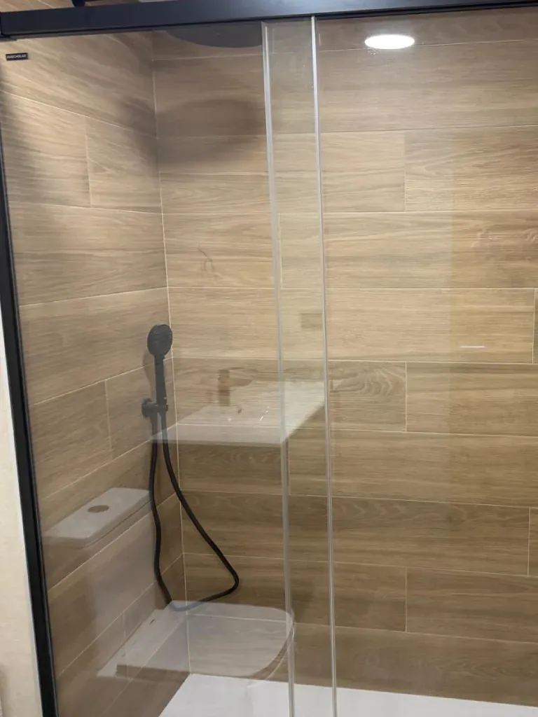 Ducha con azulejo imitación madera clara y mampara
